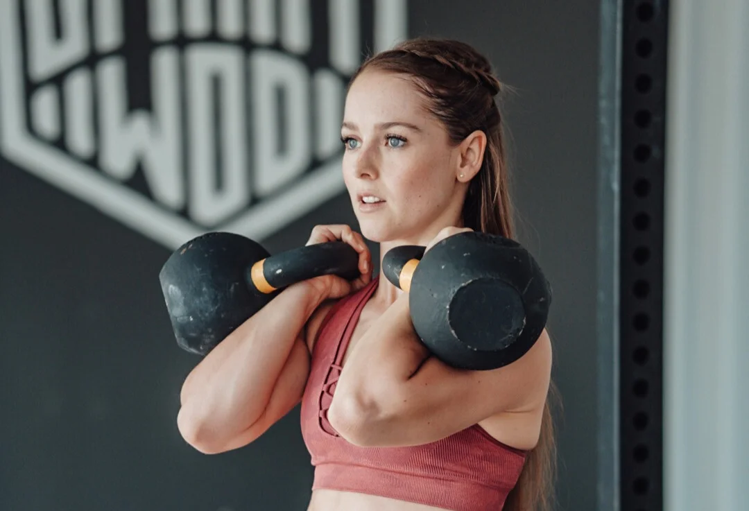 Junge SmartWOD Athletin, die zwei Kettlebells hält.