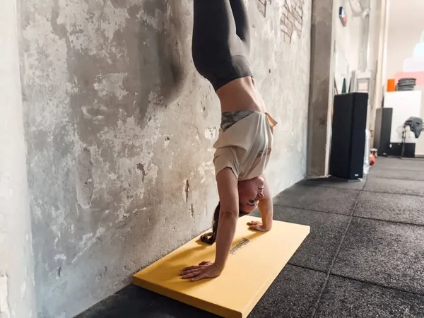 Athlete holding a handstand against the wall on a yellow mat